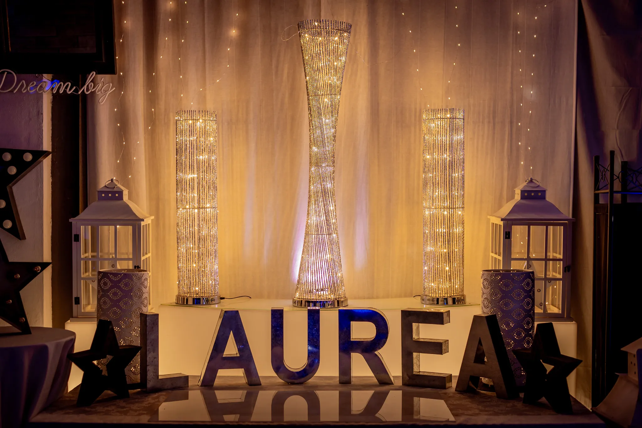 Allestimento di una festa con la parola LAUREA illuminata, lanterne bianche e torri di lucine